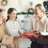 Waist up portrait of cheerful young people exchanging presents during Christmas party in cozy interior, copy space