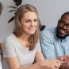 Happy smiling young blond woman talking with diverse male coworkers having break at work. Excited female colleague sharing information, news or business idea. Focus on black and caucasian workers