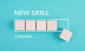 Photo of a teal background with wooden blocks arranged like a progress bar and one block offset to the right, with white text reading “NEW SKILL” above and “LOADING…..” below.
